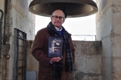 Ricardo Montés posa con un ejemplar de la Novela ante la campana Petra.